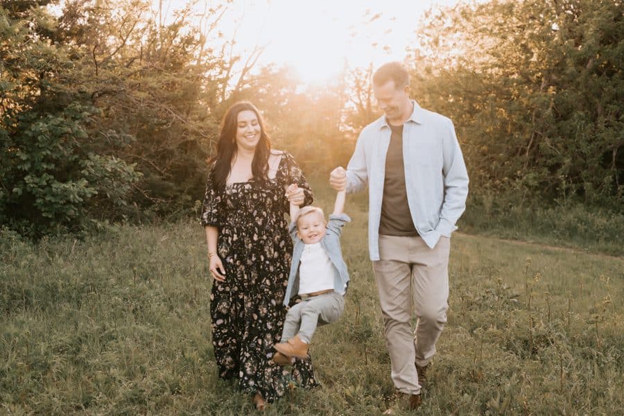 Parents Holding Sons Hands Swinging Him Back And Forth Pose For Family Photographer In Dallas