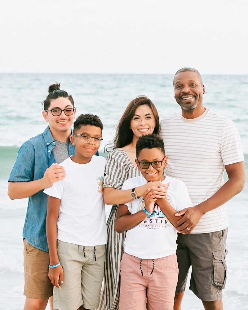 family of five stands together smiling at the beach for a family photoshoot