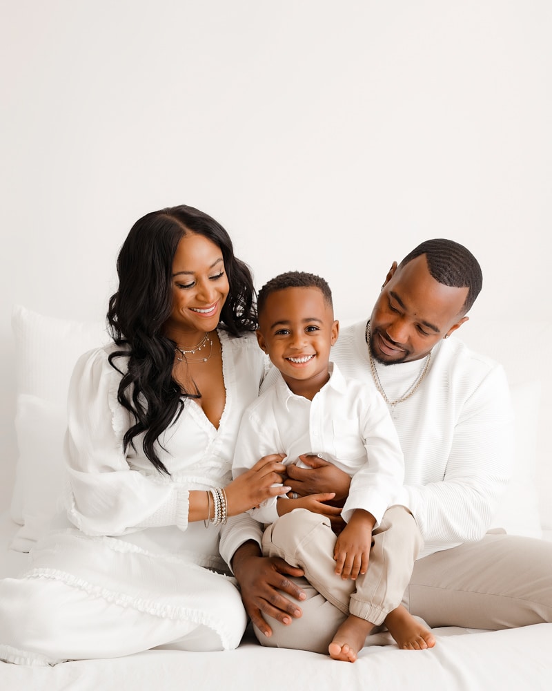 family with two kids sitting on a white bed for dallas family photographer